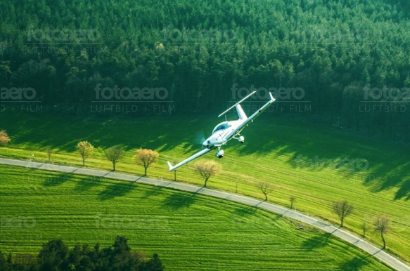 Ein Flugzeug fliegt einen groÃ?en Bogen, entlang des Waldrandes.